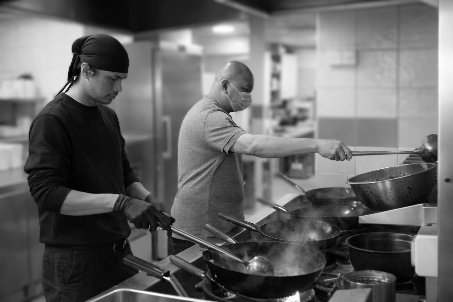 Two chefs working side by side at the woks